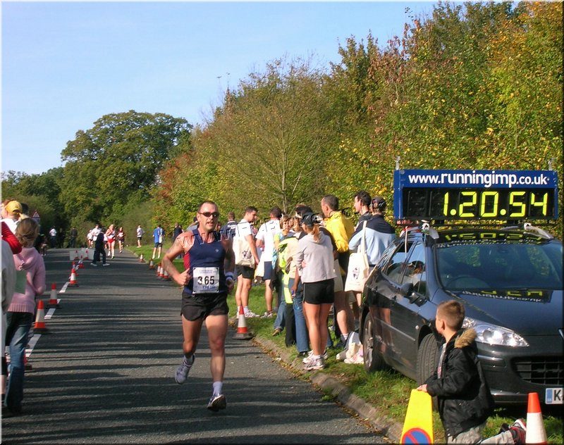 Runners finishing the 23rd Ricky Road Run beside a race clock showing 1:20:54